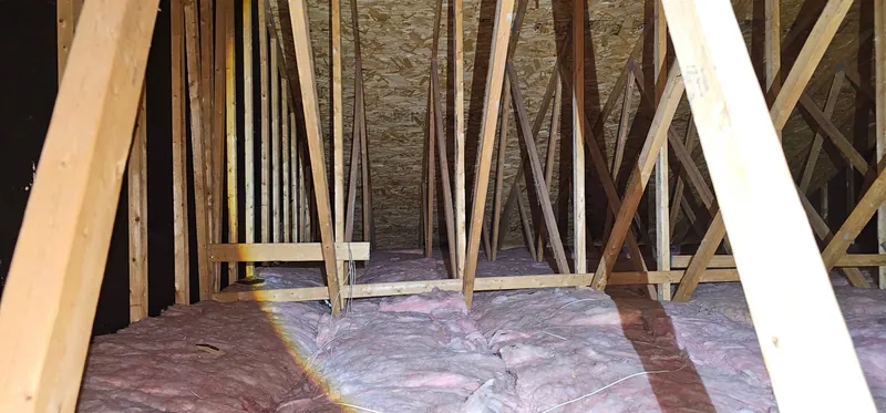 Grenier avant les travaux : anciennes nattes de laine rose, inégales et tassées, entre les fermes de toit