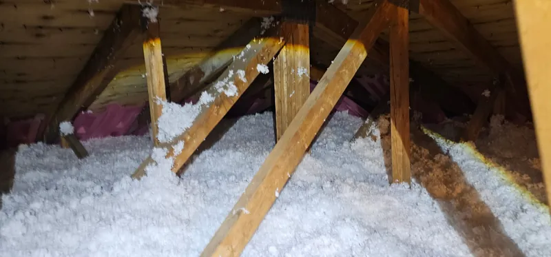Grenier après les travaux : fibre de verre soufflée blanche, épaisse et uniforme, autour des fermes de toit, déflecteurs roses au bord du toit