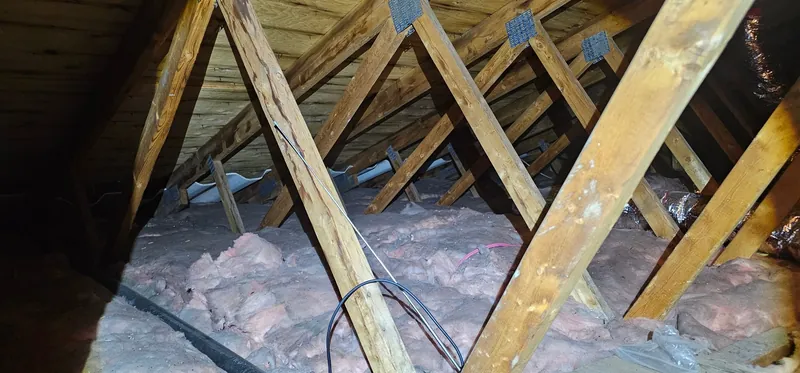 Grenier avant les travaux : anciennes nattes de laine rose, défaites et tassées, entre les fermes de toit sous le pontage en planches