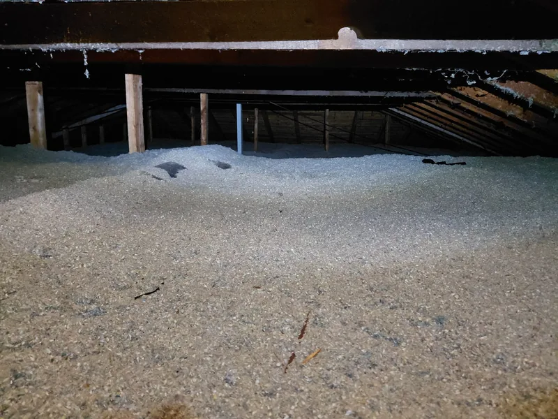 Grenier avant les travaux : vieil isolant en vrac gris-beige étalé à plat entre les poteaux de la charpente