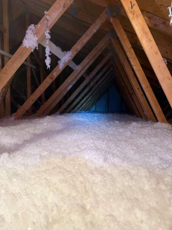 Grenier après les travaux : couche épaisse et uniforme de fibre de verre soufflée blanche sous les fermes de toit