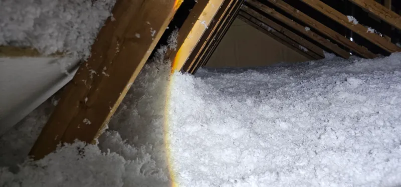 Grenier après les travaux : fibre de verre soufflée blanche, très épaisse, qui monte jusqu'aux fermes de toit, éclairée à la lampe de poche